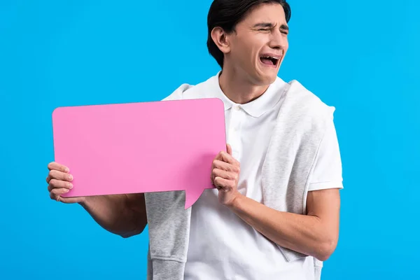 Плаче чоловік тримає рожеву бульбашку мовлення, ізольовано на синьому — стокове фото