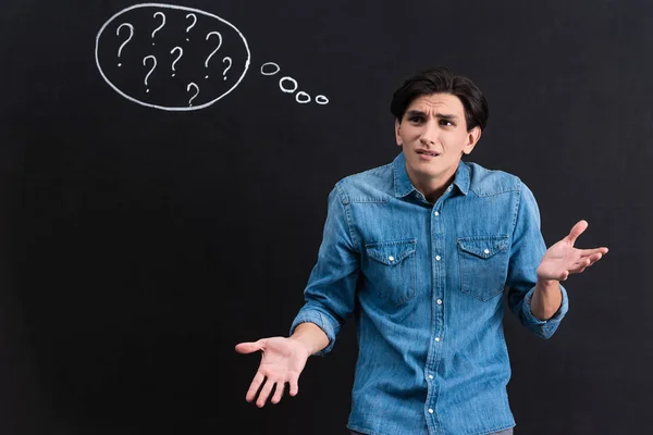 Stressé jeune homme avec des points d'interrogation dans la bulle de pensée sur tableau noir — Photo de stock