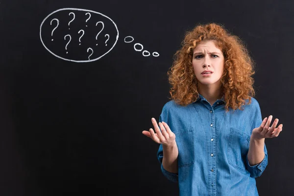 Irritated redhead girl with question marks in thought bubble on blackboard — Stock Photo