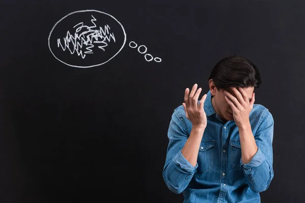 Frustrated young man with thought bubble drawing on blackboard — Stock Photo