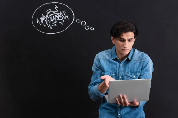 Смущенный молодой человек с помощью ноутбука, с мыслями пузырь рисования на доске — стоковое фото
