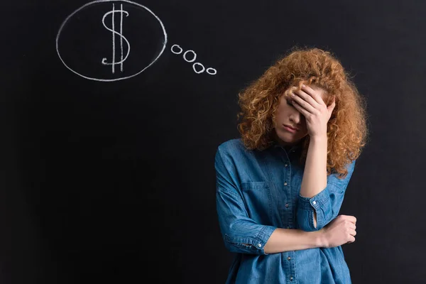 Upset pensive girl with dollar sign in thought bubble on chalkboard — Stock Photo