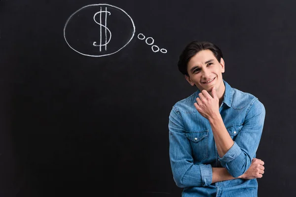 Dreamy young man with dollar in thought bubble sign on blackboard — Stock Photo