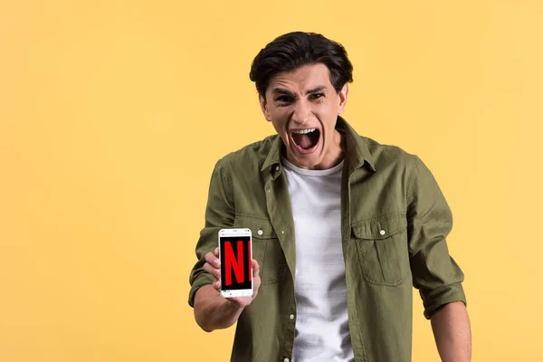 KYIV, UKRAINE - NOVEMBER 18, 2019: angry yelling man showing smartphone with netflix app on screen, isolated on yellow — Stock Photo