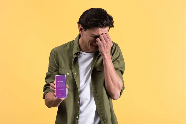 KYIV, UCRANIA - 18 de noviembre de 2019: hombre llorando mostrando el teléfono inteligente con la aplicación instagram en la pantalla, aislado en amarillo - foto de stock