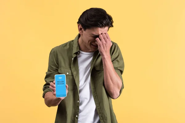 KYIV, UKRAINE - NOVEMBER 18, 2019: worried man crying and showing smartphone with skype app on screen, isolated on yellow — Stock Photo