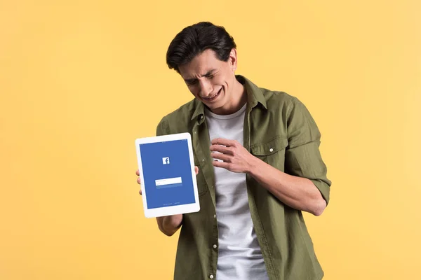 KYIV, UKRAINE - NOVEMBER 18, 2019: stressed man crying and showing digital tablet with facebook app on screen, isolated on yellow — Stock Photo