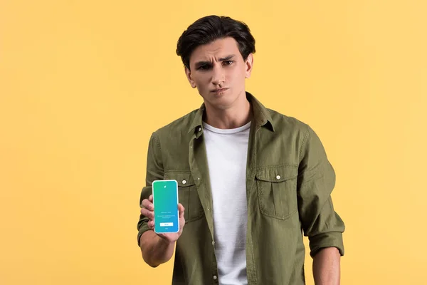 KYIV, UCRAINA - 18 NOVEMBRE 2019: uomo scettico che mostra smartphone con app twitter sullo schermo, isolato su giallo — Foto stock
