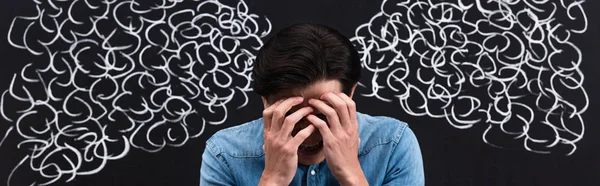 Panoramic shot of frustrated young man with steam drawing on chalkboard behind — Stock Photo