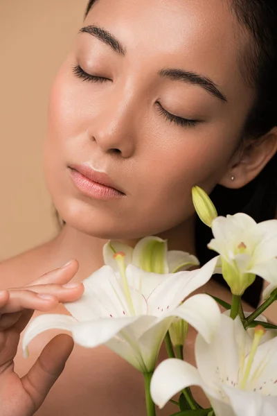 Hermosa chica asiática desnuda con los ojos cerrados y lirios blancos aislados en beige - foto de stock