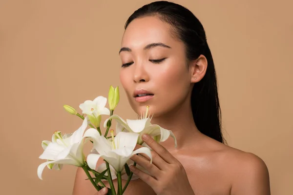 Beautiful naked asian girl with white lilies isolated on beige — Stock Photo