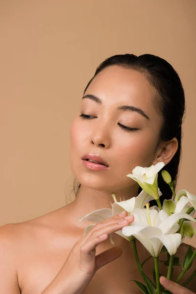 Beautiful naked asian girl with white lilies looking away isolated on beige — Stock Photo