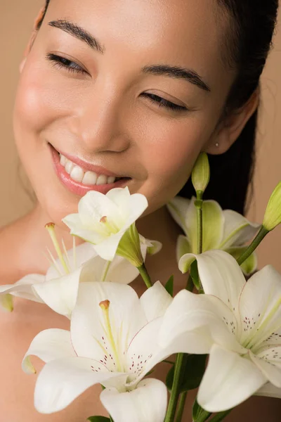 Happy beautiful naked asian girl with white lilies isolated on beige — Stock Photo