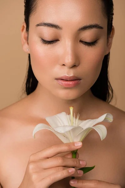 Красивая голая азиатская девушка, смотрящая на белую лилию, изолированную от бежевого — стоковое фото