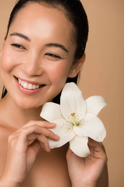 Sonriendo hermosa desnuda chica asiática sosteniendo lirio blanco aislado en beige - foto de stock