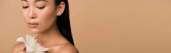 Hermosa chica asiática desnuda sosteniendo lirio blanco aislado en beige, tiro panorámico - foto de stock