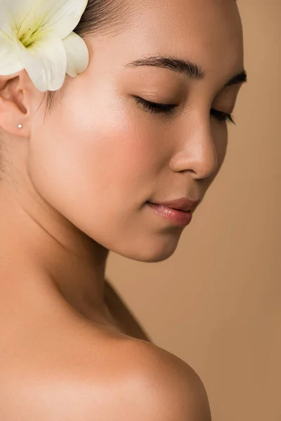 Beautiful naked asian girl with white lily in hair isolated on beige — Stock Photo