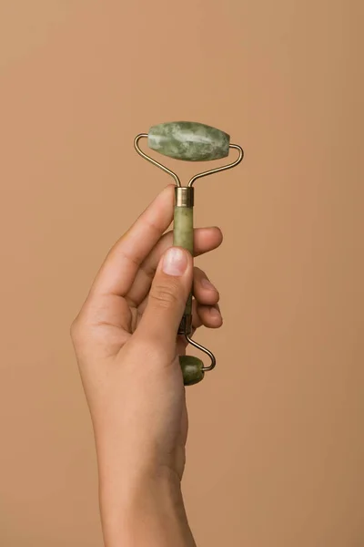 Cropped view of woman holding jade roller isolated on beige — Stock Photo