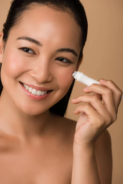 Sourire belle nu asiatique fille en utilisant oeil rouleau isolé sur beige — Photo de stock