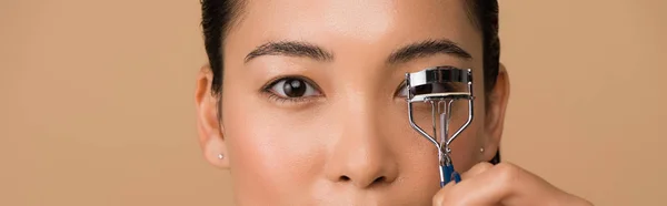 Vue recadrée de belle fille asiatique en utilisant des bigoudis de cils isolés sur beige, vue panoramique — Stock Photo