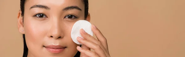 Beautiful asian girl holding cotton pad on face isolated on beige, panoramic shot — Stock Photo