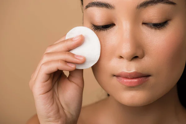 Beautiful naked asian girl holding cotton pad on face isolated on beige — Stock Photo