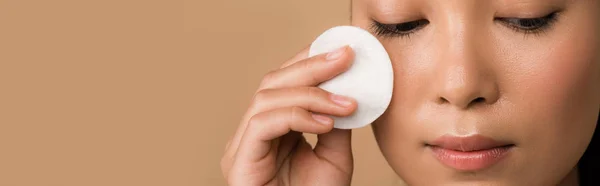 Beautiful asian girl holding cotton pad on face isolated on beige, panoramic shot — Stock Photo