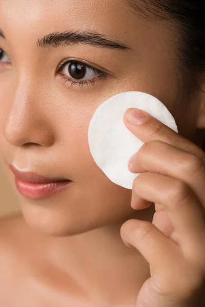 Close up view of beautiful naked asian girl holding cotton pad on face isolated on bege — Fotografia de Stock