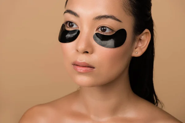 Beautiful naked asian girl with black hydrogel eye patches under eyes isolated on beige — Stock Photo