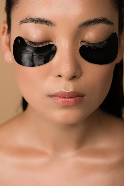 Bonito nu ásia menina com preto hidrogel olho remendos sob fechado olhos isolado no bege — Fotografia de Stock