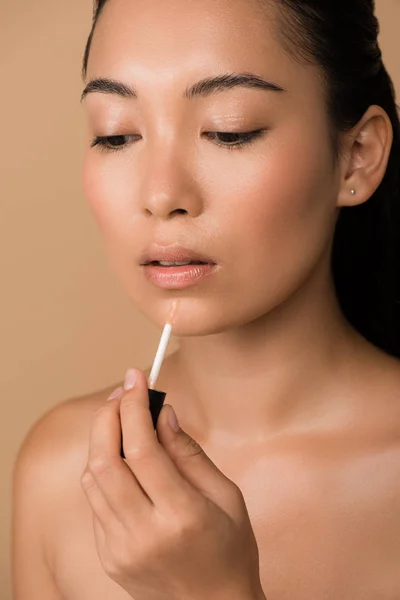 Beautiful naked asian girl appying lip gloss on lips isolated on beige — Stock Photo