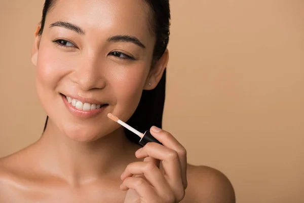 Smiling beautiful naked asian girl appying lip gloss on lips isolated on beige — Stock Photo