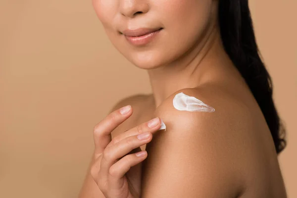 Cropped view of beautiful naked asian girl with cosmetic cream on shoulder isolated on beige — Stock Photo