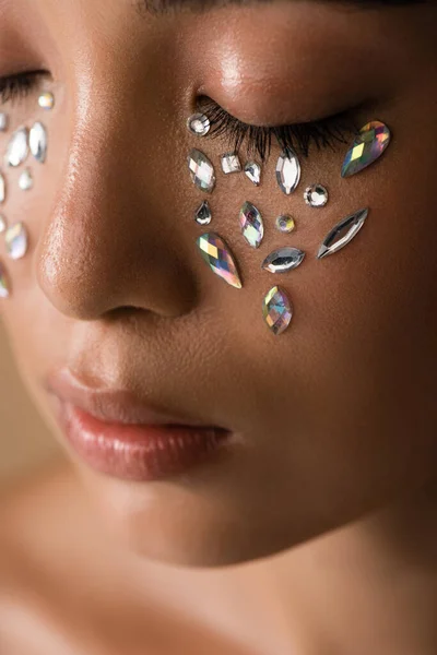 Close up view of beautiful naked asian girl with closed eyes and rhinestones on face isolated on beige — Stock Photo
