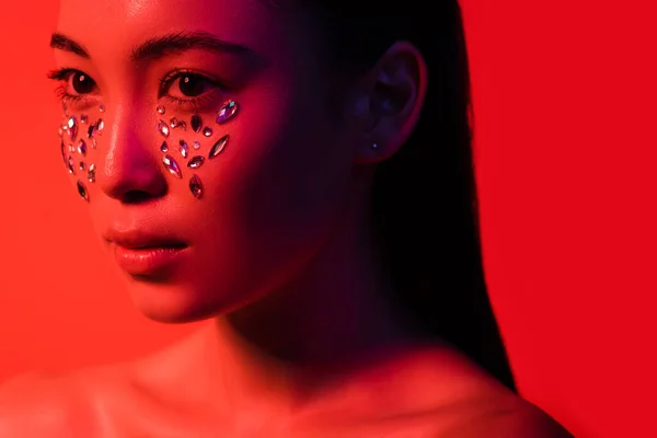 Hermosa chica asiática desnuda con pedrería en la cara aislada en rojo - foto de stock