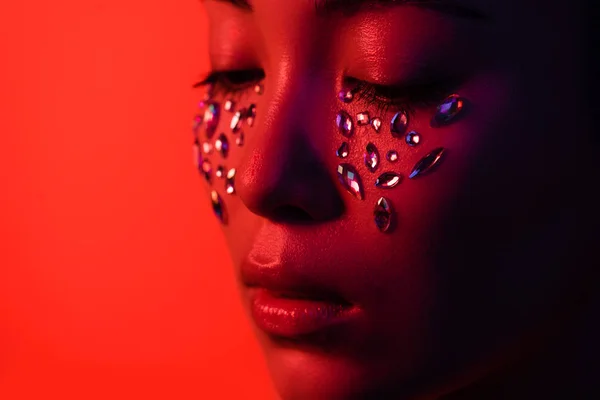 Hermosa chica asiática con diamantes de imitación en la cara aislado en rojo - foto de stock