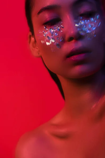 Belle fille asiatique nue avec strass sur le visage isolé sur rouge, flou de mouvement — Photo de stock