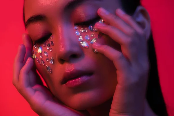 Beautiful asian girl touching face with rhinestones isolated on red, motion blur — Stock Photo