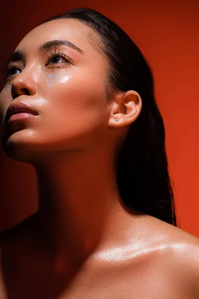 Low angle view of beautiful naked asian girl with silver sparkles on face on red — Stock Photo