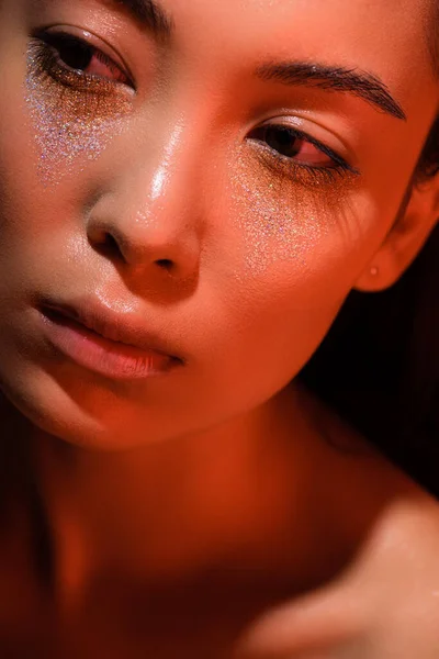 De cerca vista de hermosa chica asiática desnuda con destellos de plata en la cara en la iluminación roja - foto de stock