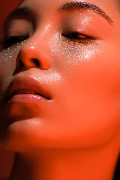 Close up view of beautiful asian girl with silver sparkles on face in red lighting — Stock Photo