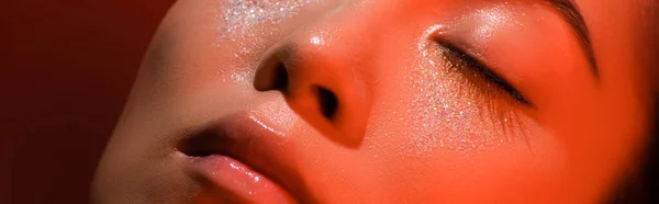 Nahaufnahme der schönen asiatischen Mädchen mit geschlossenen Augen und silbernen Funkeln im Gesicht und geschlossenen Augen in rotem Licht, Panoramaaufnahme — Stockfoto