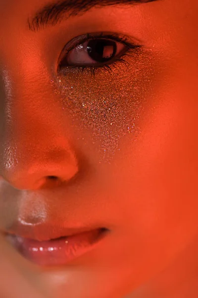 Крупный план красивой девушки с серебряными искрами на лице при красном освещении — стоковое фото