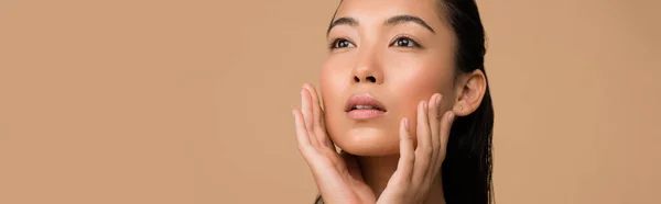 Bella ragazza asiatica toccare il viso e guardando lontano isolato sul beige, colpo panoramico — Foto stock