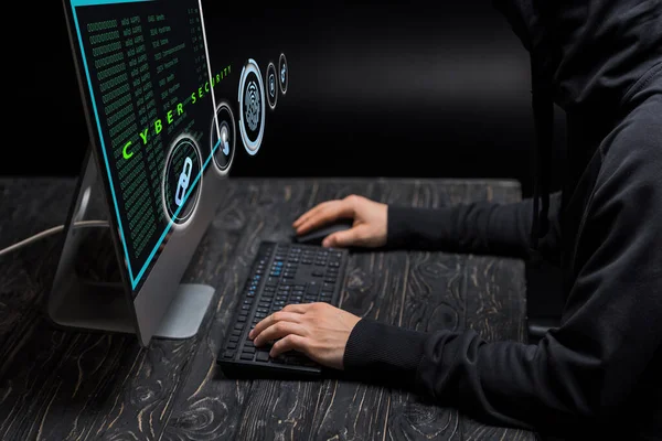 Cropped view of hacker typing on computer keyboard near computer monitor with cyber security lettering on black — Stock Photo