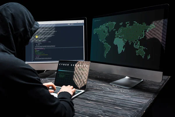 Hacker using laptop with cyber security lettering on screen near computer monitors on black — Stock Photo