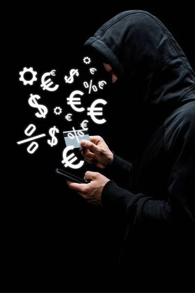 Hacker en la capucha y la máscara con el teléfono inteligente y la celebración de tarjetas de crédito cerca de signos de dinero aislados en negro - foto de stock