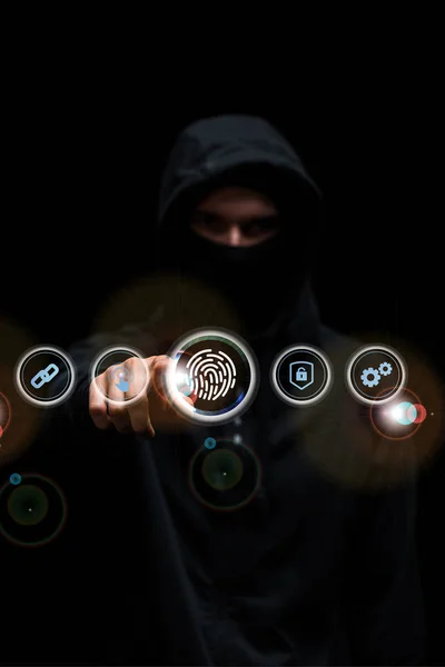 Selective focus of hacker in hood pointing with finger at fingerprint web icon on black — Stock Photo
