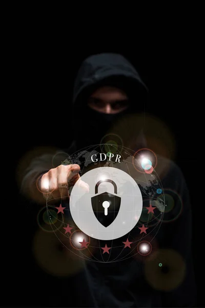 Selective focus of hacker in hood pointing with finger at gdpr lettering on black — Stock Photo
