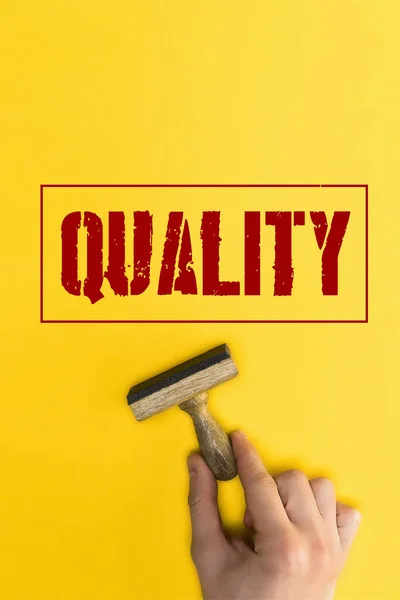 Top view of man holding stamp near quality lettering on yellow — Stock Photo